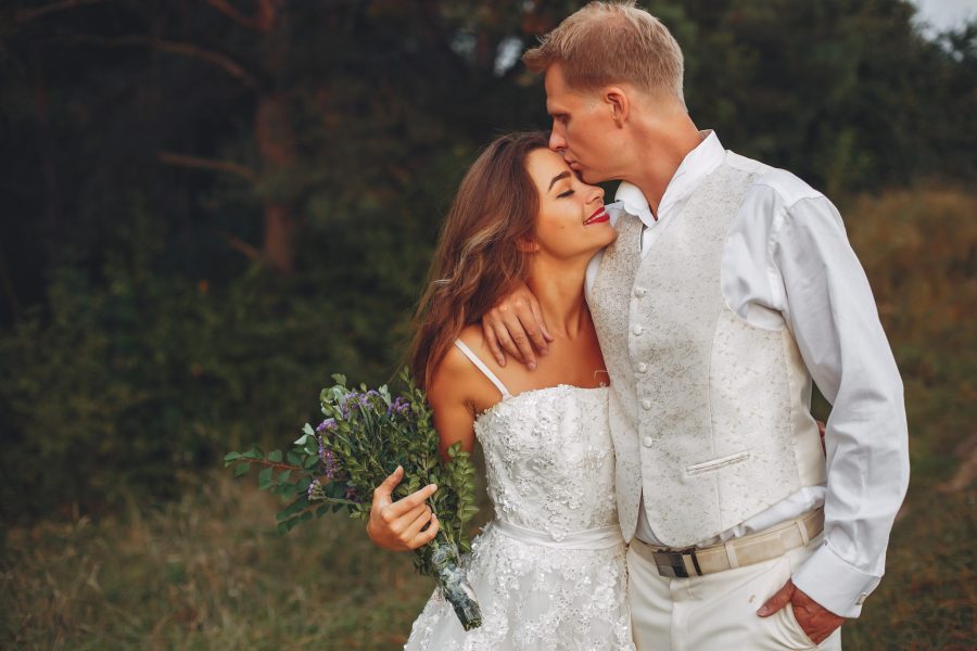 Beautiful bride in a white dress. Couple in a summer field. Woman with a bouquet of flowers